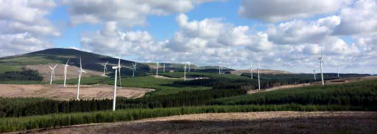 Ladera llena de molinos de aerogeneradores produciendo energía eléctrica y con nubes al fondo